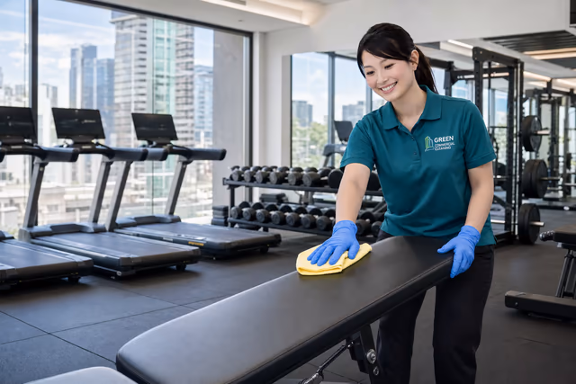 Green Commercial Cleaning employee wiping a bench in a modern gym